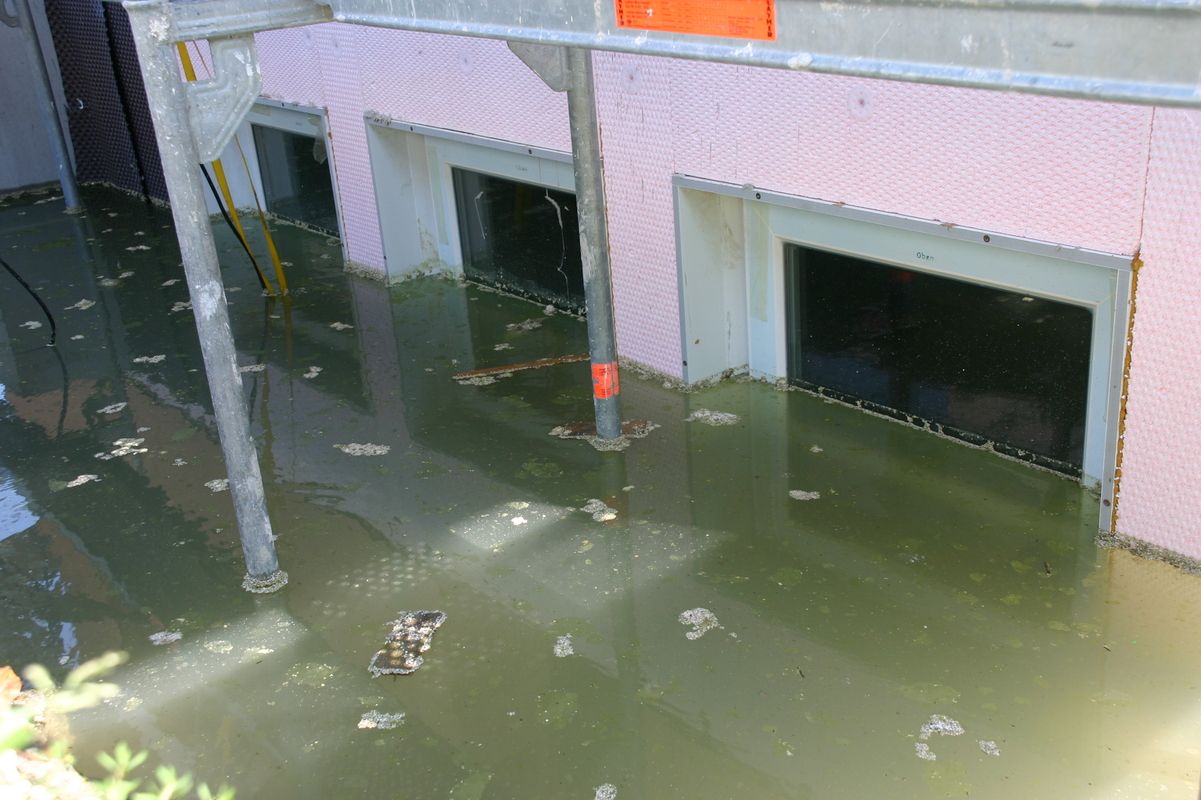 Wasser steht hoch vor einem Gebäude mit zwei kleinen Fenstern im Kellerbereich